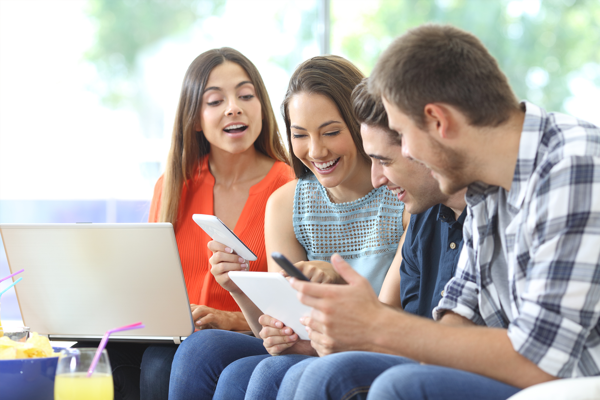 Four friends sharing mobile devices and laptop together, representing ElektraFi's refer a friend program for internet serv...
